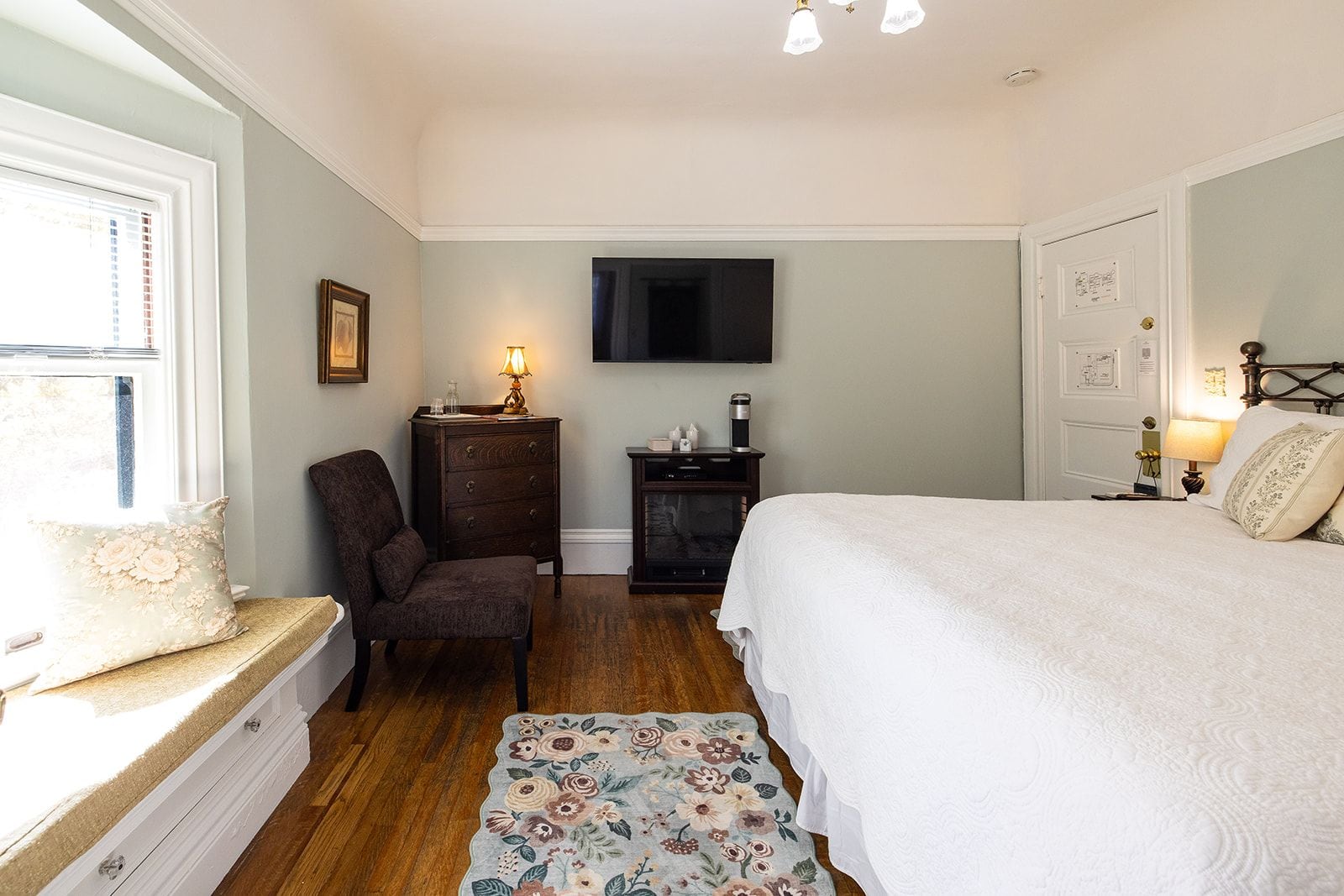 A bedroom with a bed, a chair, a dresser, a television, and a small table with a lamp.