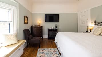 A bedroom with a bed, a chair, a dresser, a television, and a small table with a lamp.