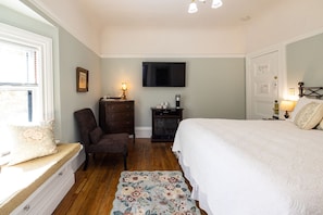 A bedroom with a bed, a chair, a dresser, a television, and a small table with a lamp. - Napa Inn (Napa)