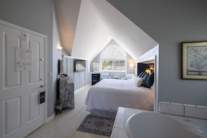 Een slaapkamer met een groot bed, een open haard, een raam met zonwering en een badkamer met een bad.