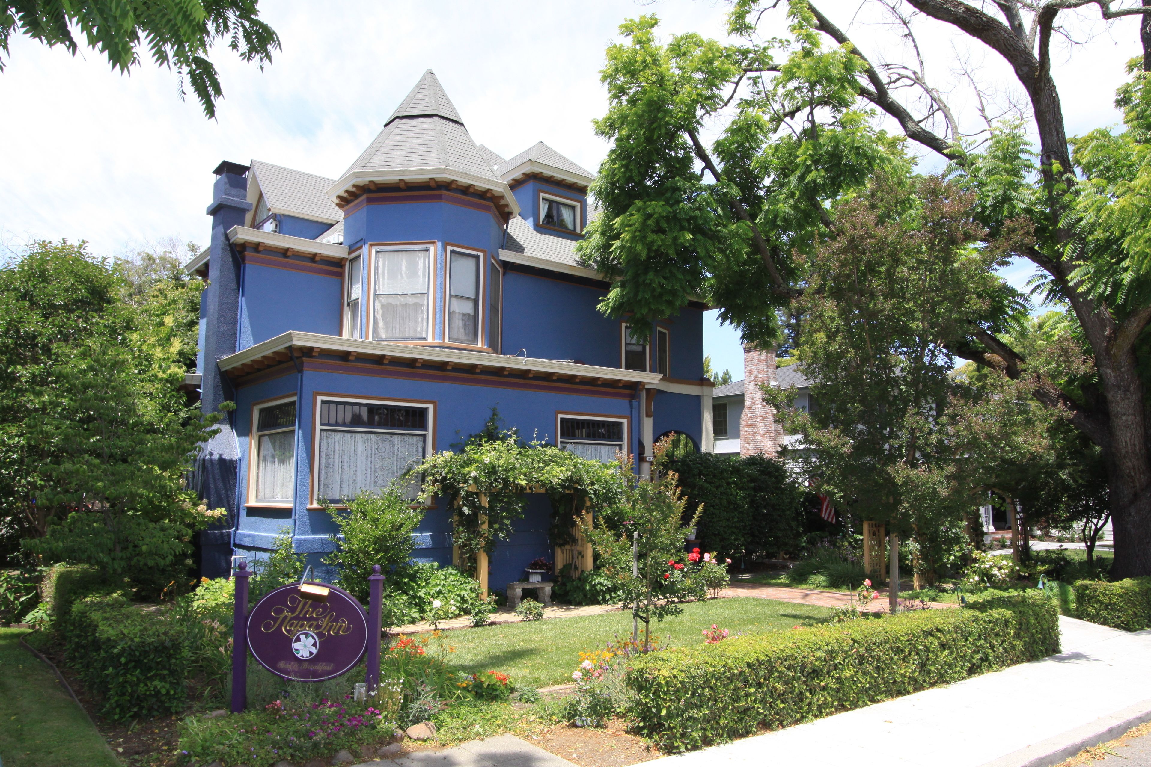 Una casa de estilo victoriano con una torre destacada, rodeada de jardines cuidados y un cielo despejado.