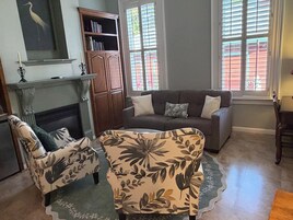 Uma sala de estar com lareira, um sofá, duas poltronas e uma estante de livros.