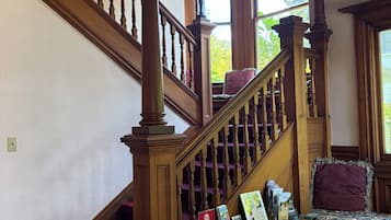 A wooden staircase with a decorative railing, a desk with various items, and a window with a view of greenery.