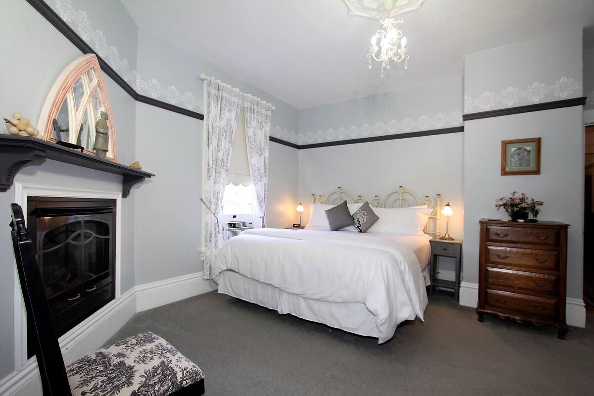 A bedroom with a bed, bedside table, dresser, and a fireplace.