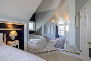 Un dormitorio con cama, mesita de noche, lámpara y baño con bañera, espejo y toallero.