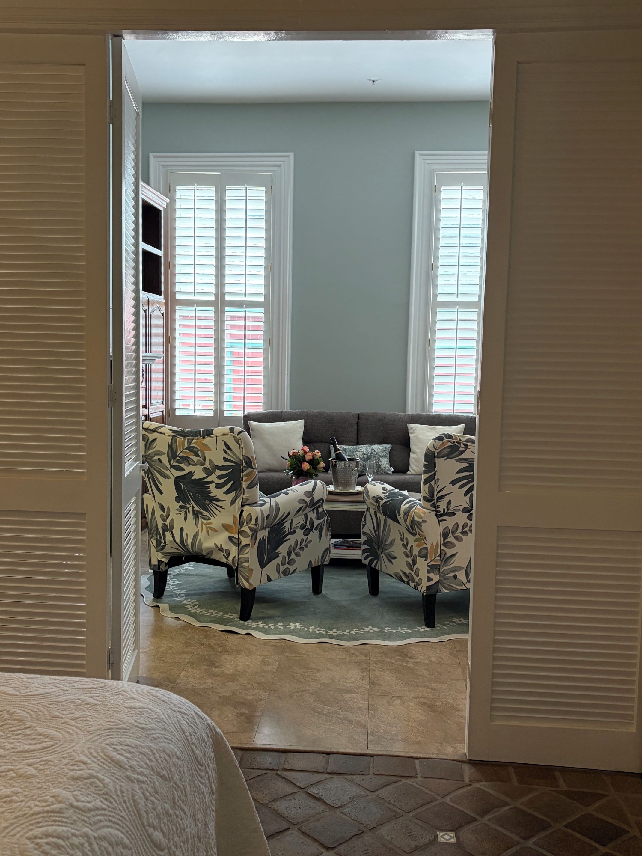 A room with a bed, a sofa, two armchairs, a coffee table, and a window with blinds.