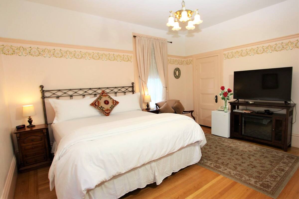A bedroom with a bed, nightstands, a TV, a small table with flowers, and a rug.
