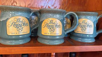 Quatre tasses ornées du logo « The Napa Inn » sont posées sur une étagère en bois.