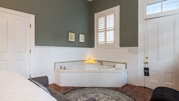 Un dormitorio con una cama grande, una zona de estar con una silla, una bañera y una puerta con ventana.