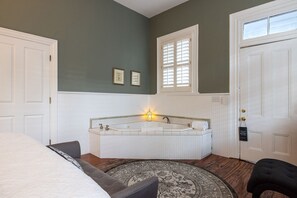 Un dormitorio con una cama grande, una zona de estar con una silla, una bañera y una puerta con ventana.