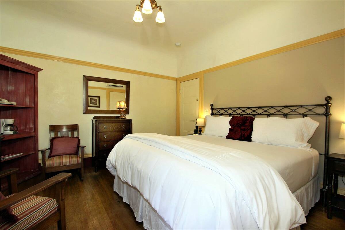 A hotel room with a large bed, a wooden chair, a dresser, and a bookshelf.
