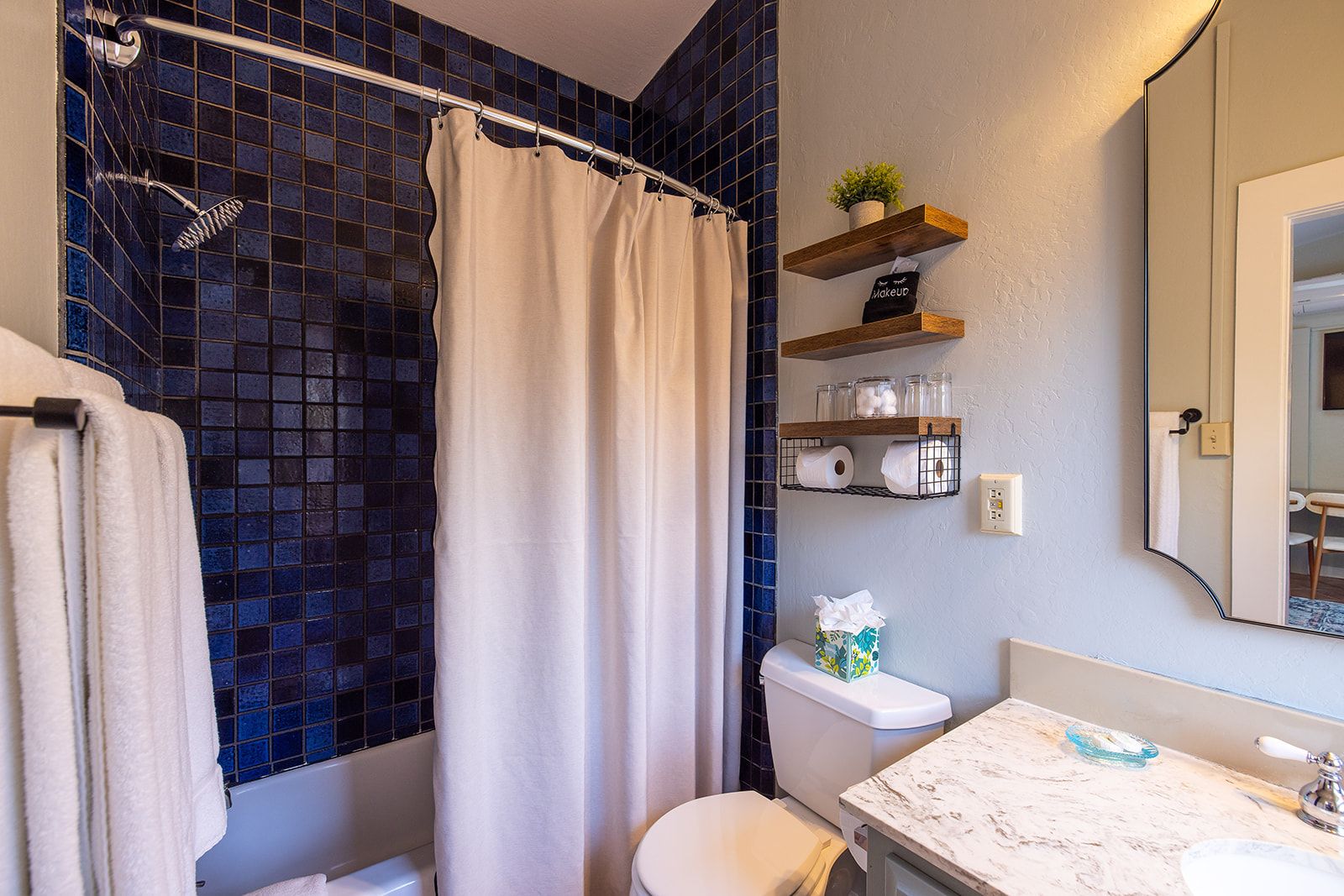 Een badkamer met douchegordijn, toilet, wastafel met een marmeren blad en planken met toiletartikelen.