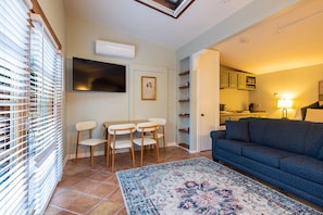 Una sala de estar con sofá, una mesa de comedor con sillas, televisor y una cocina al fondo.