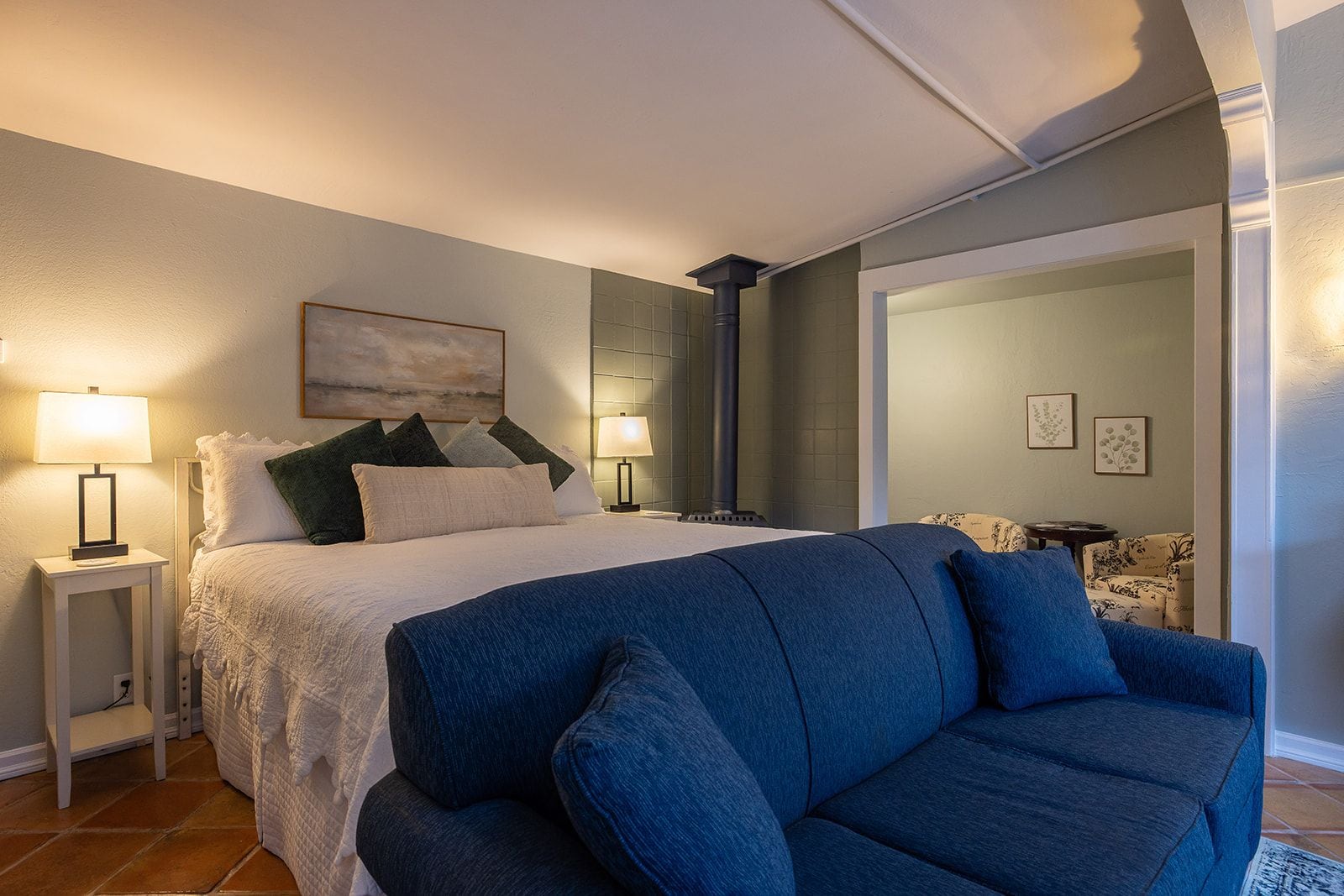 A bedroom with a bed, bedside tables, a blue sofa, and a fireplace.