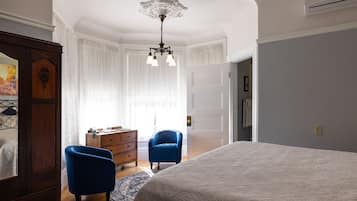 Une chambre à coucher avec un grand lit, deux fauteuils bleus, une commode en bois et un lustre.