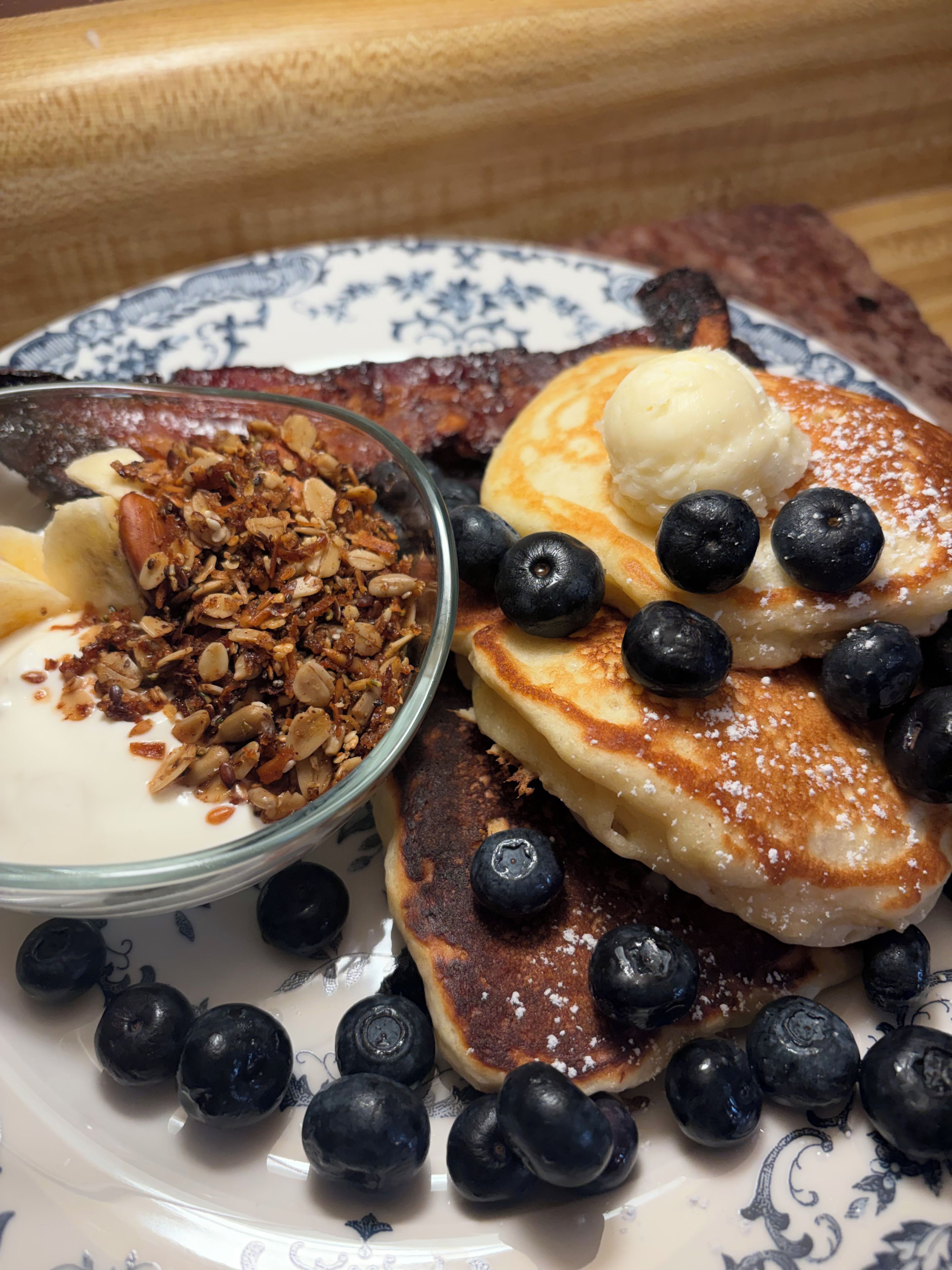 Um prato com panquecas, amoras e uma tigela de granola com iogurte.