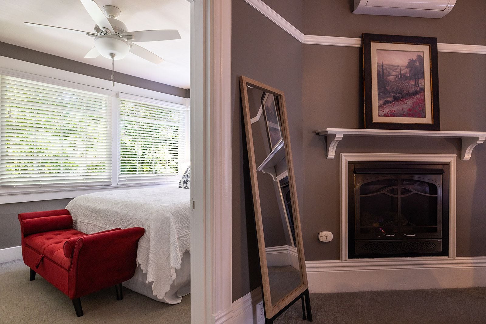 A room with a bed, a red chair, a fireplace, and a framed picture on the wall.