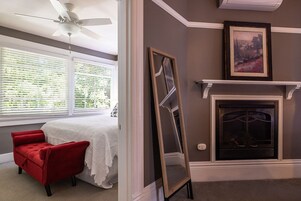 Una habitación con cama, una silla roja, una chimenea y un cuadro en la pared.