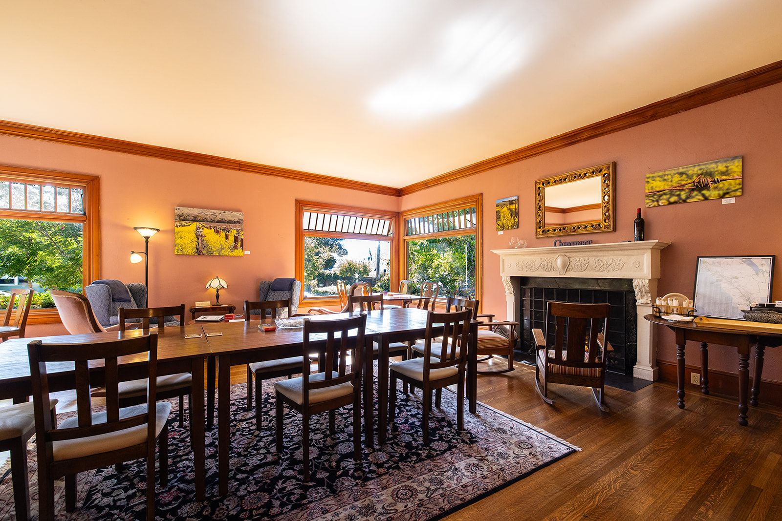 A dining room with a large wooden table, multiple chairs, a fireplace, and large windows.