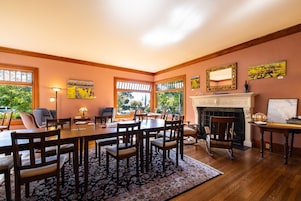 Comedor con gran mesa de madera, varias sillas, chimenea y ventanas amplias.