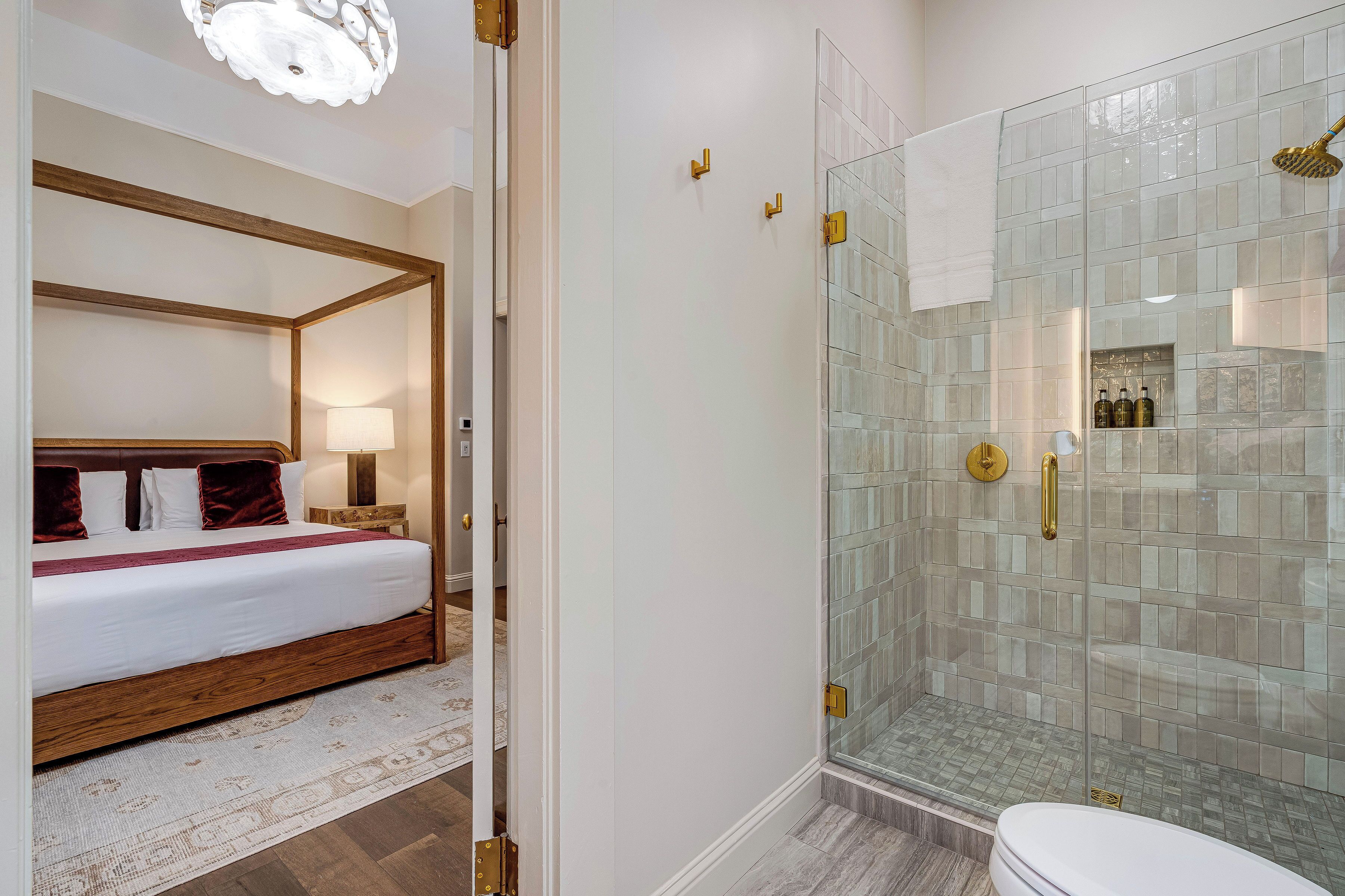A hotel room with a four-poster bed, a glass-enclosed shower, and a white toilet.