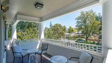 A covered balcony with white railings, two chairs, and a small table.