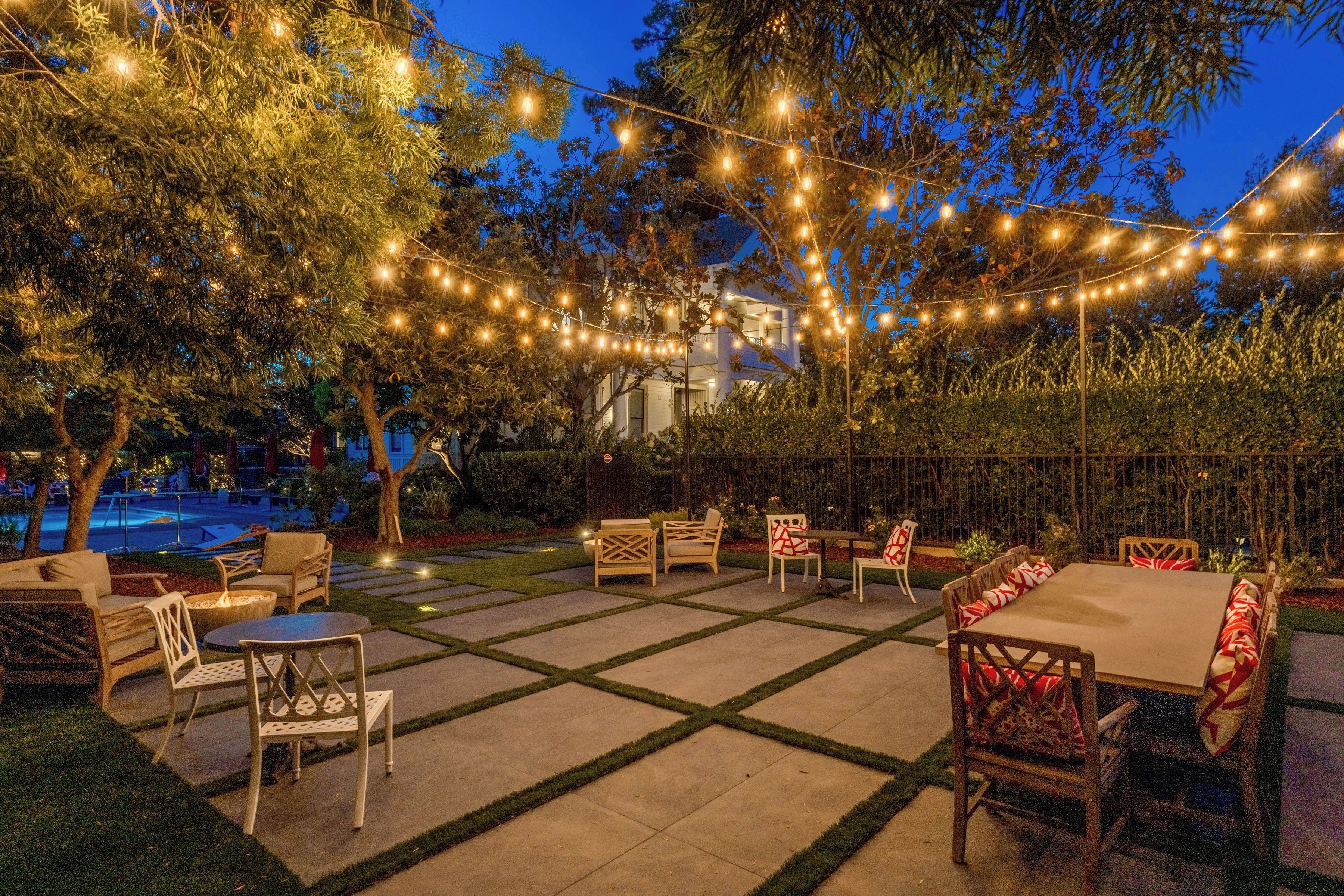 An outdoor patio area with string lights, seating arrangements, and a pool in the background.