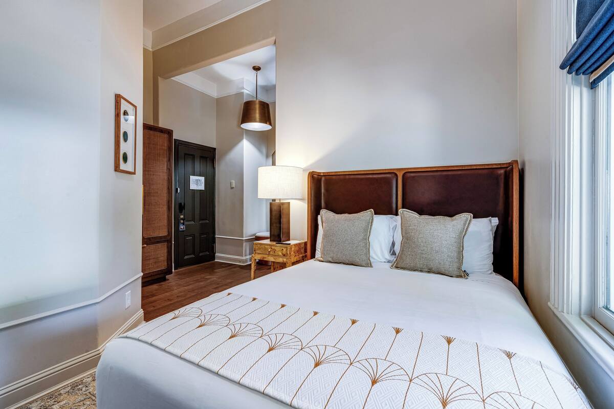 A hotel room with a large bed, a nightstand, a lamp, and a door leading to another room.