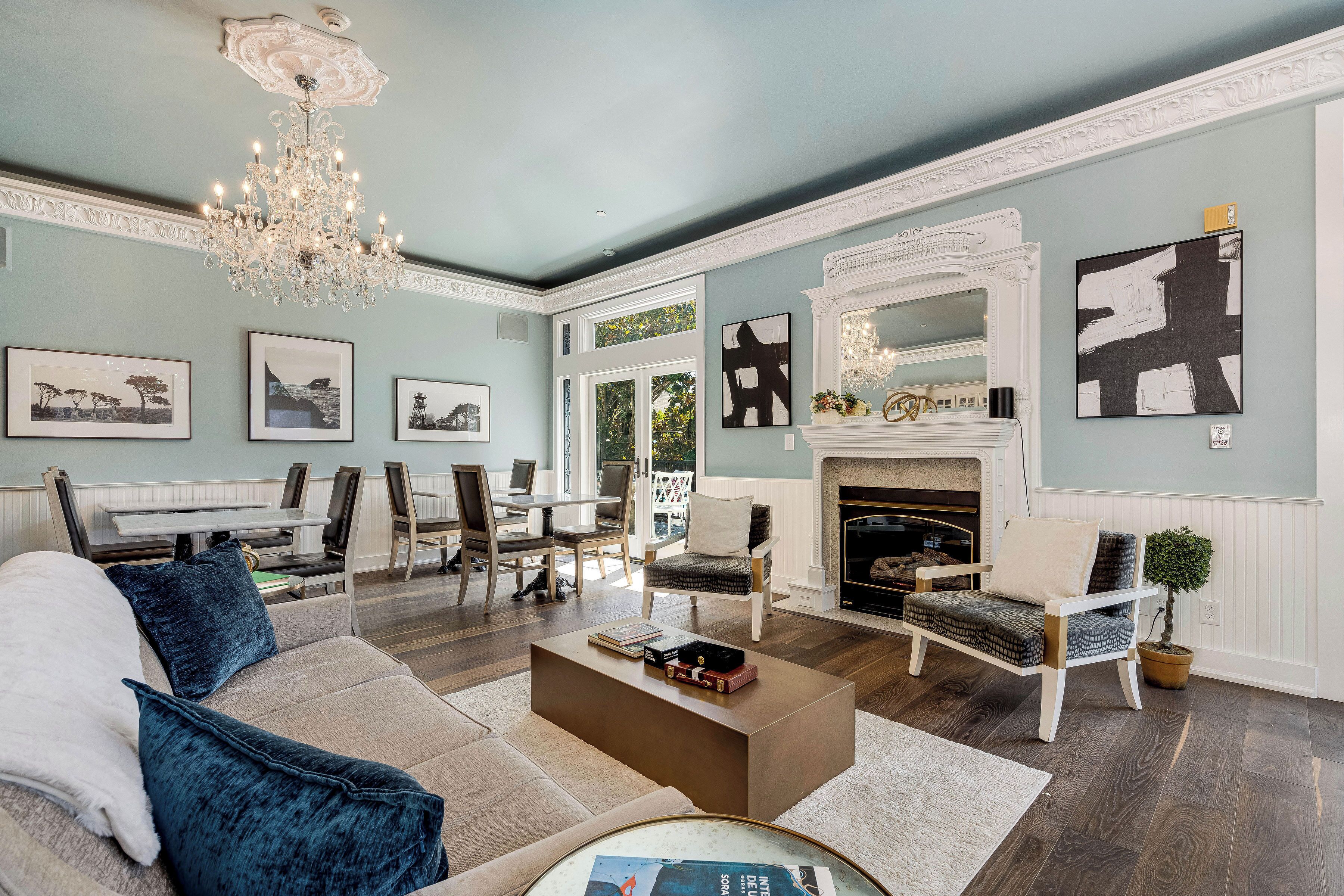 A spacious living room with a chandelier, a fireplace, and a dining area with chairs and a table.