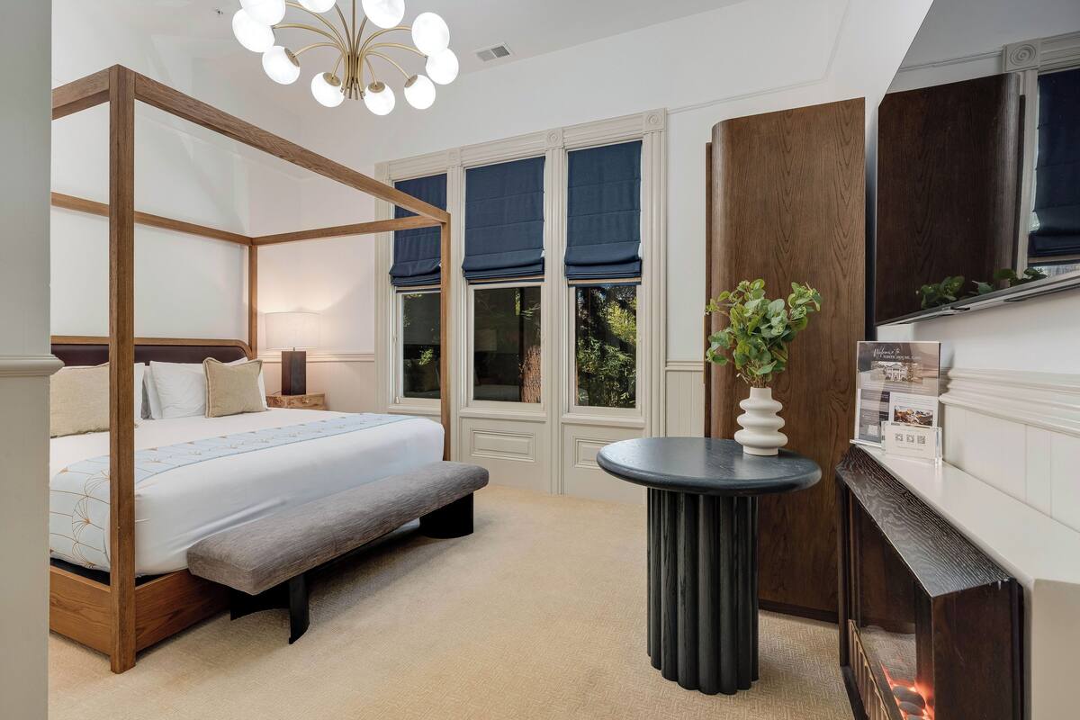 A bedroom with a four-poster bed, a bench, a round table, and a fireplace.