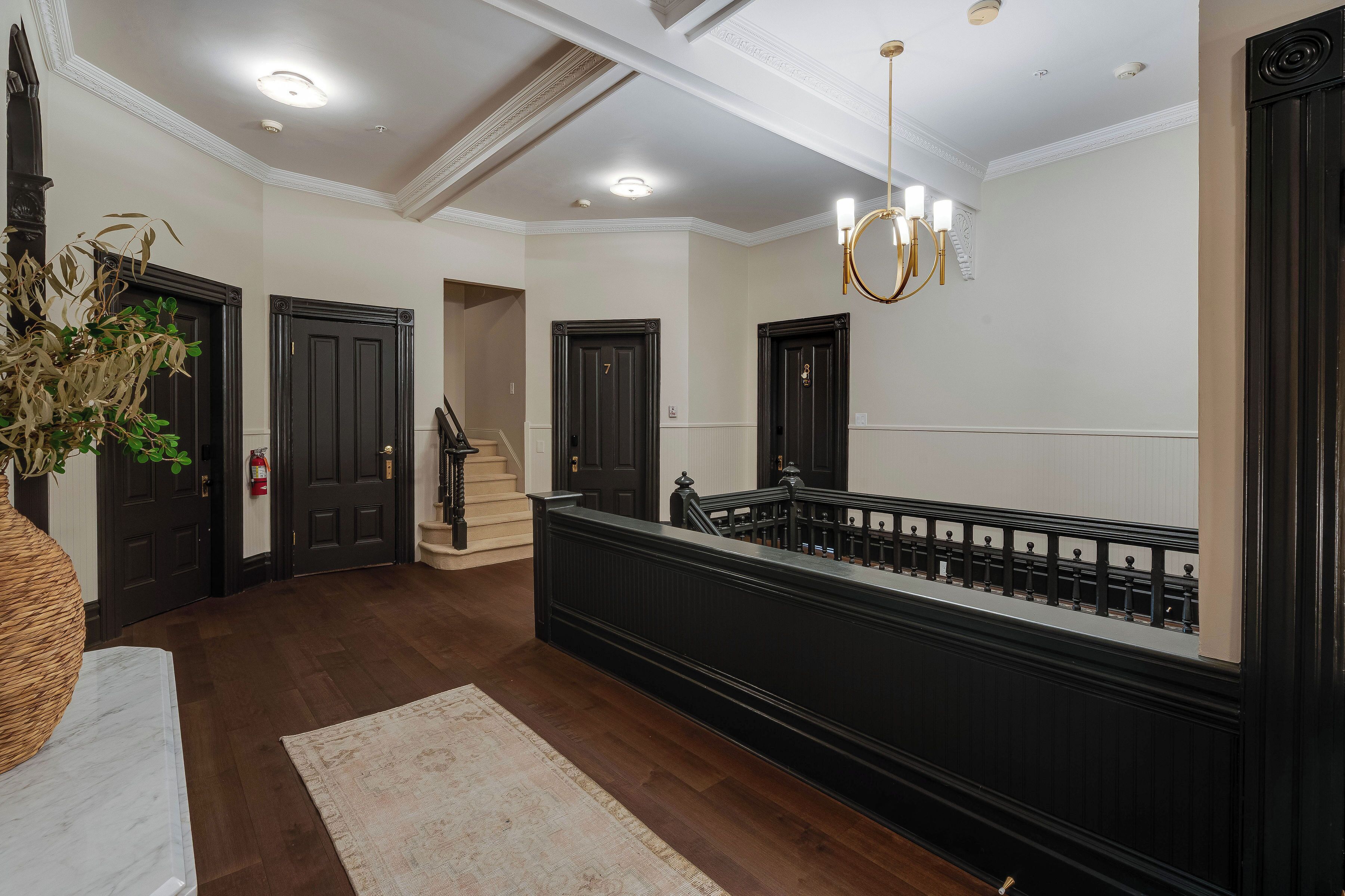 Un vaste hall d’entrée avec un parquet en bois foncé, une colonne en marbre et une balustrade noire.