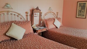 A bedroom with two beds, each with patterned bedding and pillows. There is a dresser with a mirror and a lamp between the beds. - The Mendocino Hotel and Garden Suites (Mendocino)