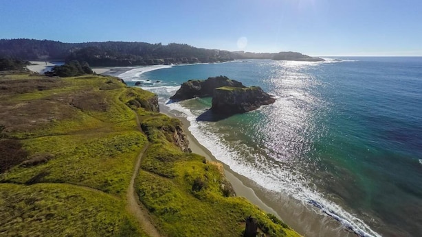 Un paysage côtier avec un sentier bien défini menant à la plage, entouré de collines verdoyantes et de formations rocheuses.