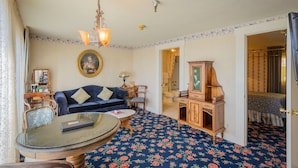 Une pièce avec un tapis à motifs floraux bleus, un canapé bleu foncé, une table basse ronde en verre, un meuble en bois et un lustre.