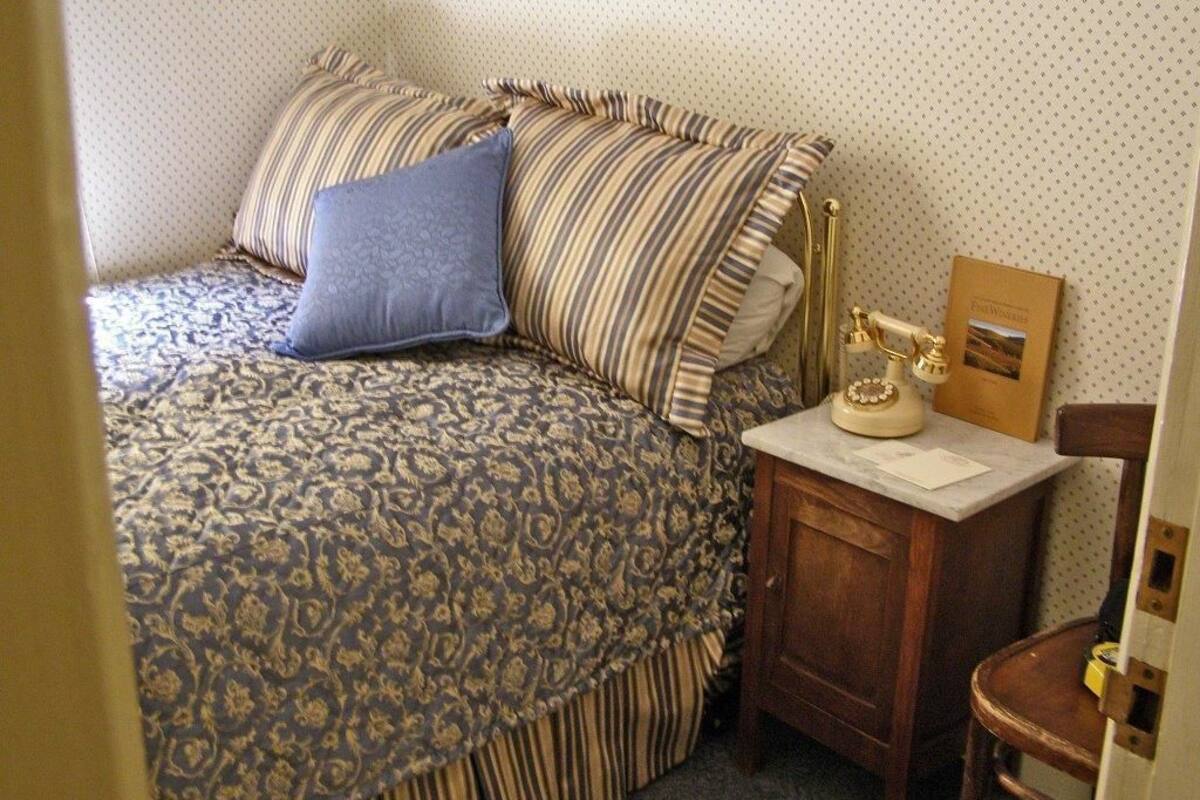 Ein Schlafzimmer mit einem gemusterten Bett, gestreiften Kissen, einem Nachttisch mit Lampe und einem gerahmten Bild an der Wand.
