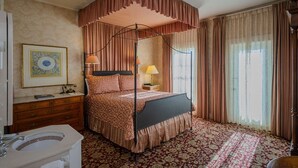 Un lit à baldaquin, une table de chevet avec une lampe, un tableau encadré au mur et un tapis à motifs.