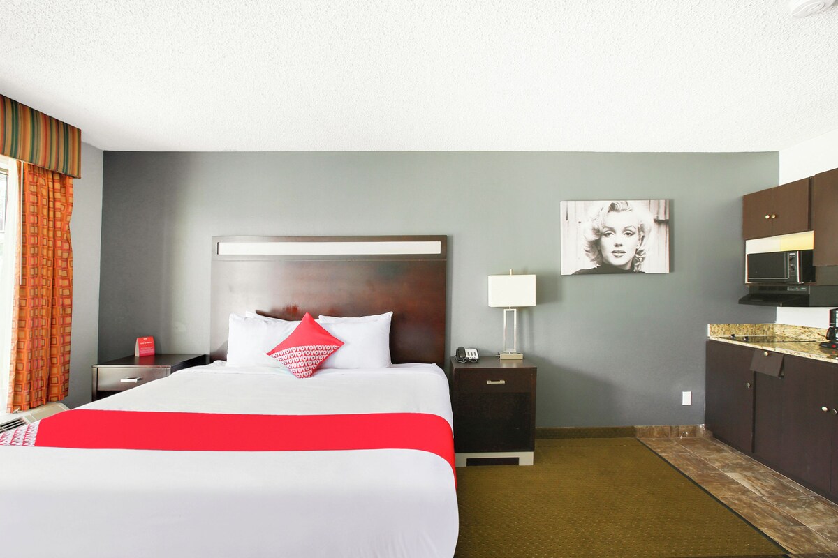 Habitación de hotel con cama, mesitas de noche, lámpara, microondas y un cuadro en la pared.