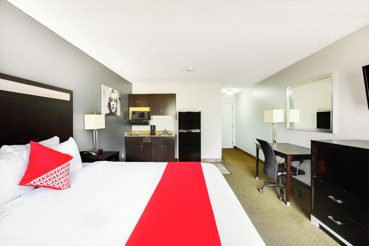 Habitación de hotel con cama, escritorio, silla, armario, espejo, kitchenette y baño.