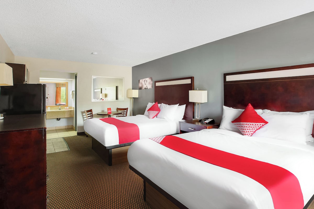 A hotel room with two beds, a desk, a chair, a television, and a bathroom visible through an open door.