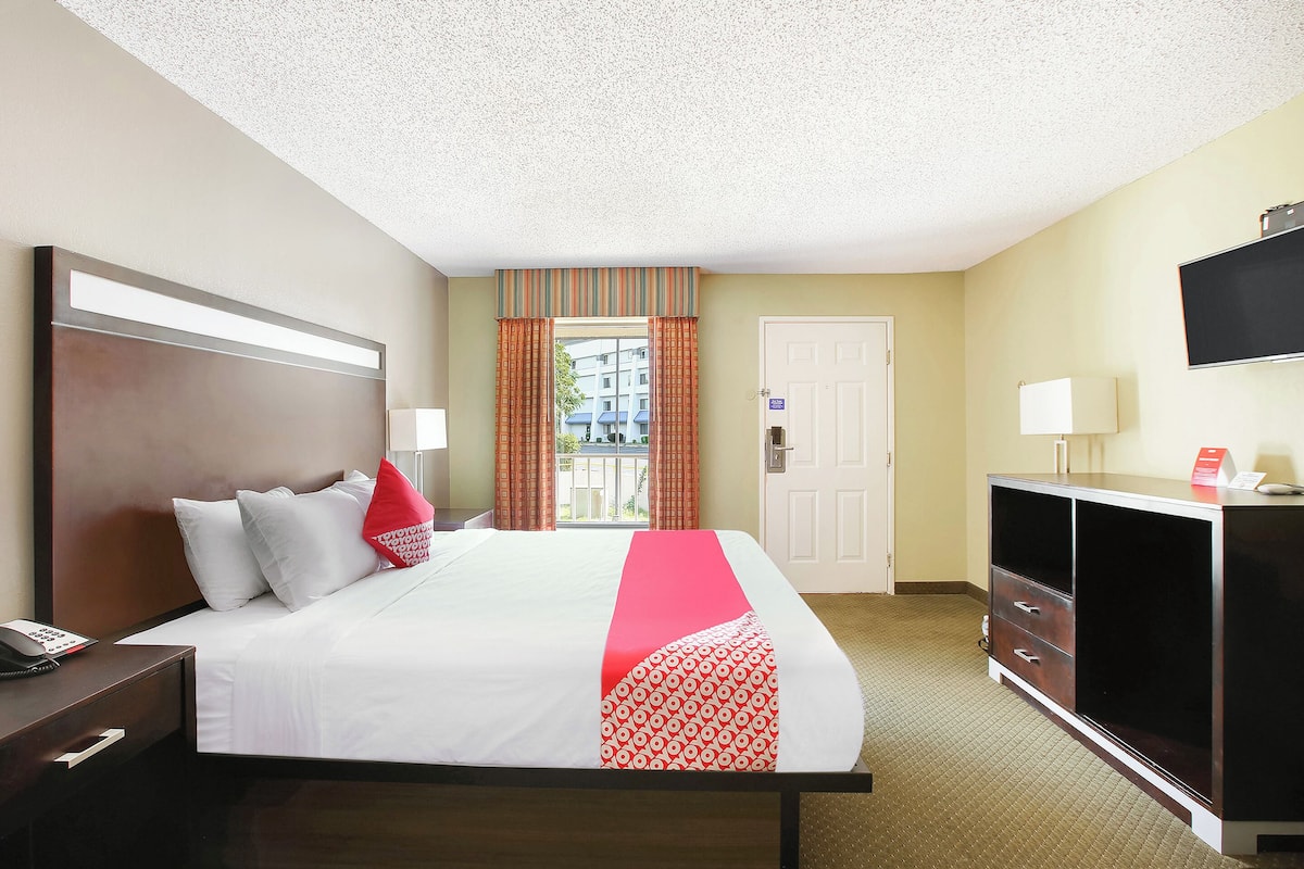 A hotel room with a bed, bedside table, TV, wardrobe, and a window with curtains.