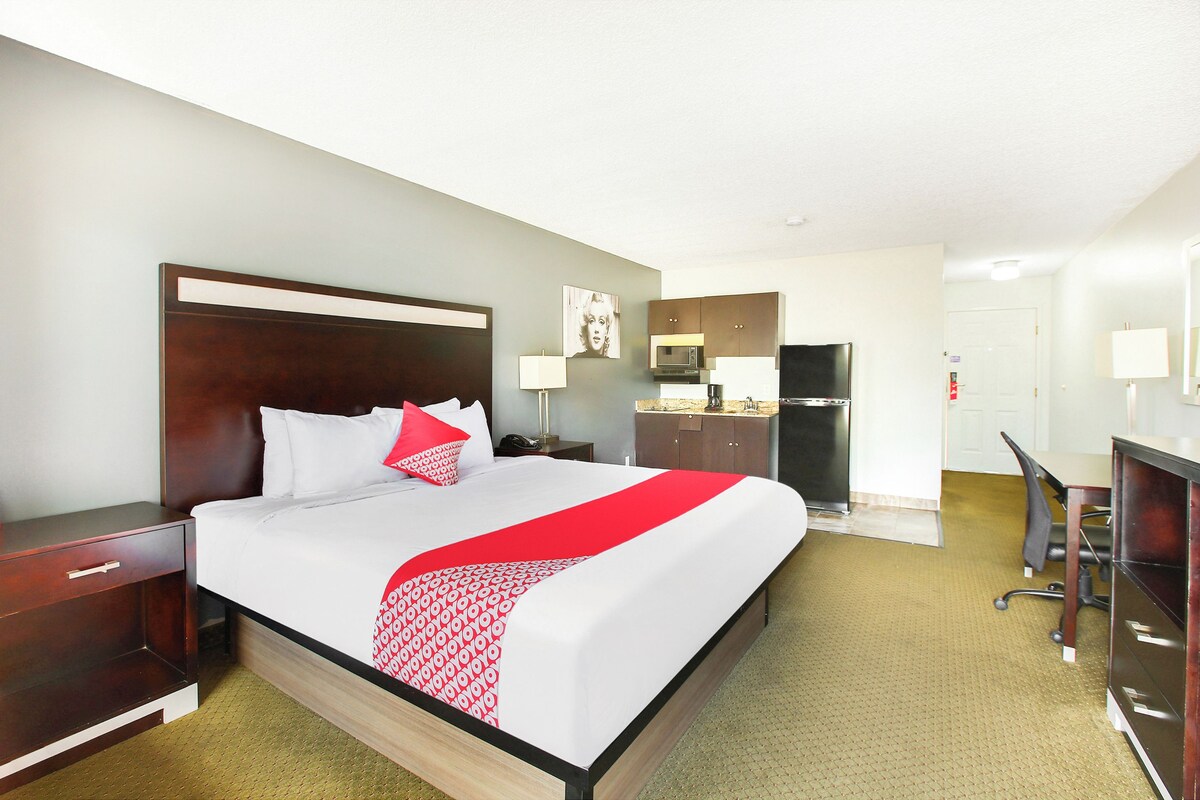 A hotel room with a large bed, a desk, a chair, a microwave, and a refrigerator.