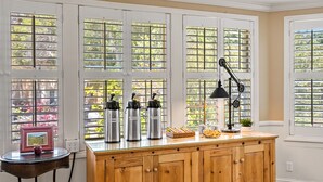A kitchen with a wooden cabinet, a coffee maker, a lamp, and a window with blinds.