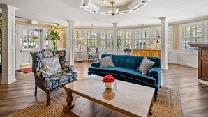 A spacious living room with a blue sofa, patterned armchair, and a coffee table with a vase of red flowers. - Apple Farm (San Luis Obispo)