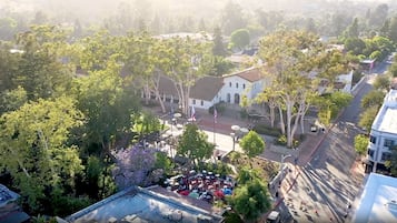 An aerial view of a town with a central white building, surrounded by trees and a street with parked cars.