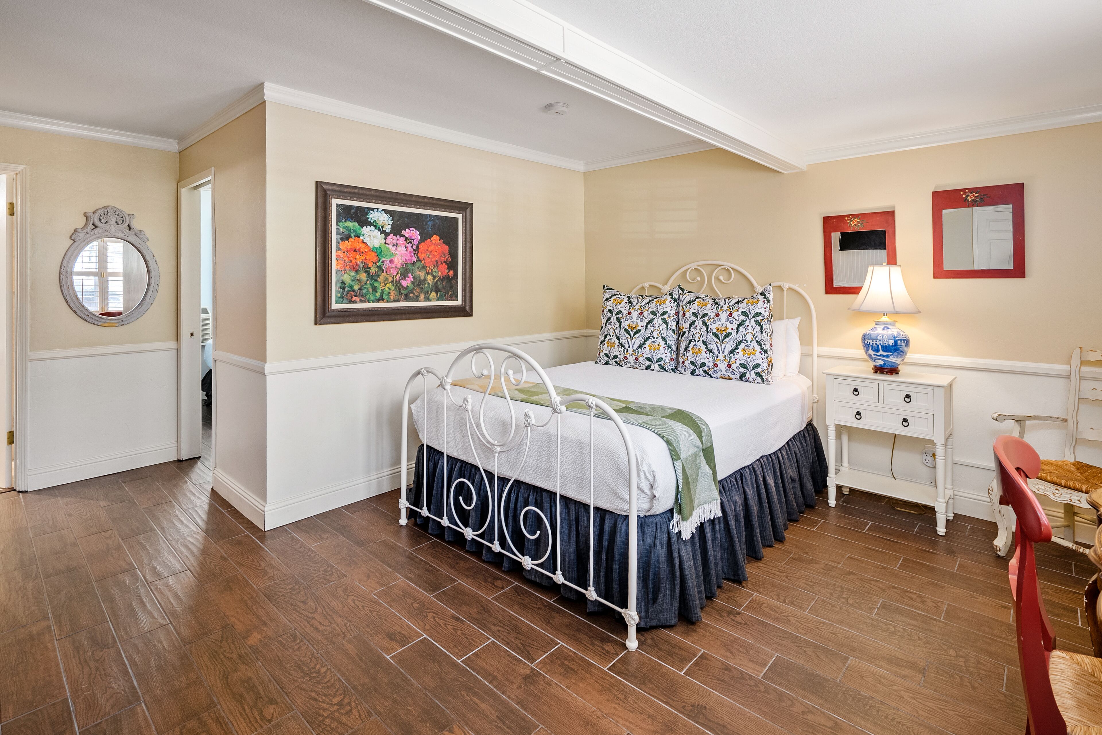 A bedroom with a bed, a nightstand, a lamp, a chair, and a painting on the wall.