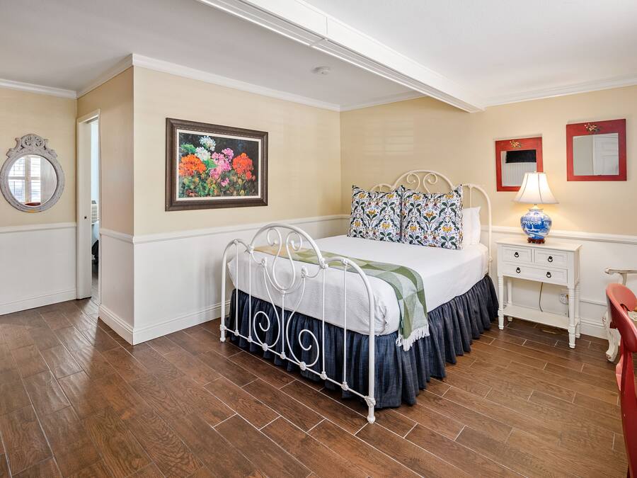 A bedroom with a bed, a nightstand, a lamp, a chair, and a painting on the wall.