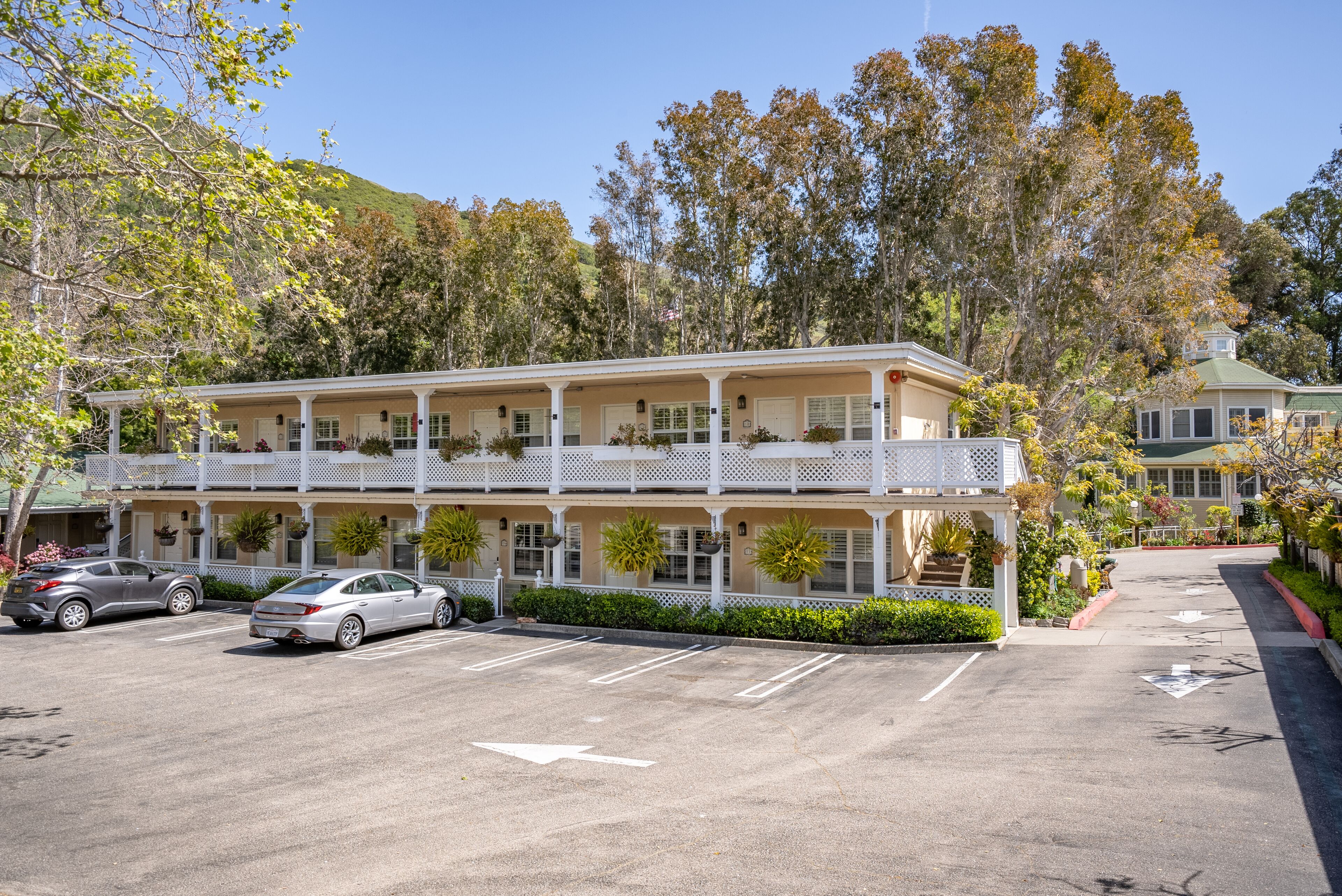 A two-story hotel with a balcony on the second floor, parking lot, and surrounding trees.