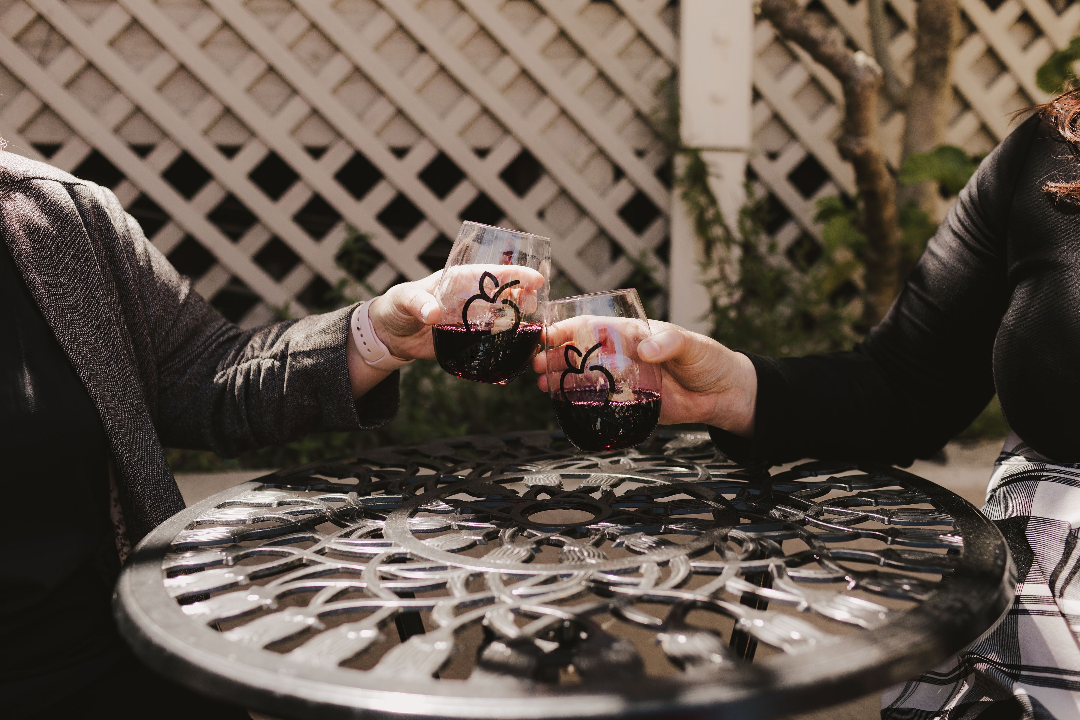 Two people toasting with glasses of red wine at a round metal table with a lattice design.