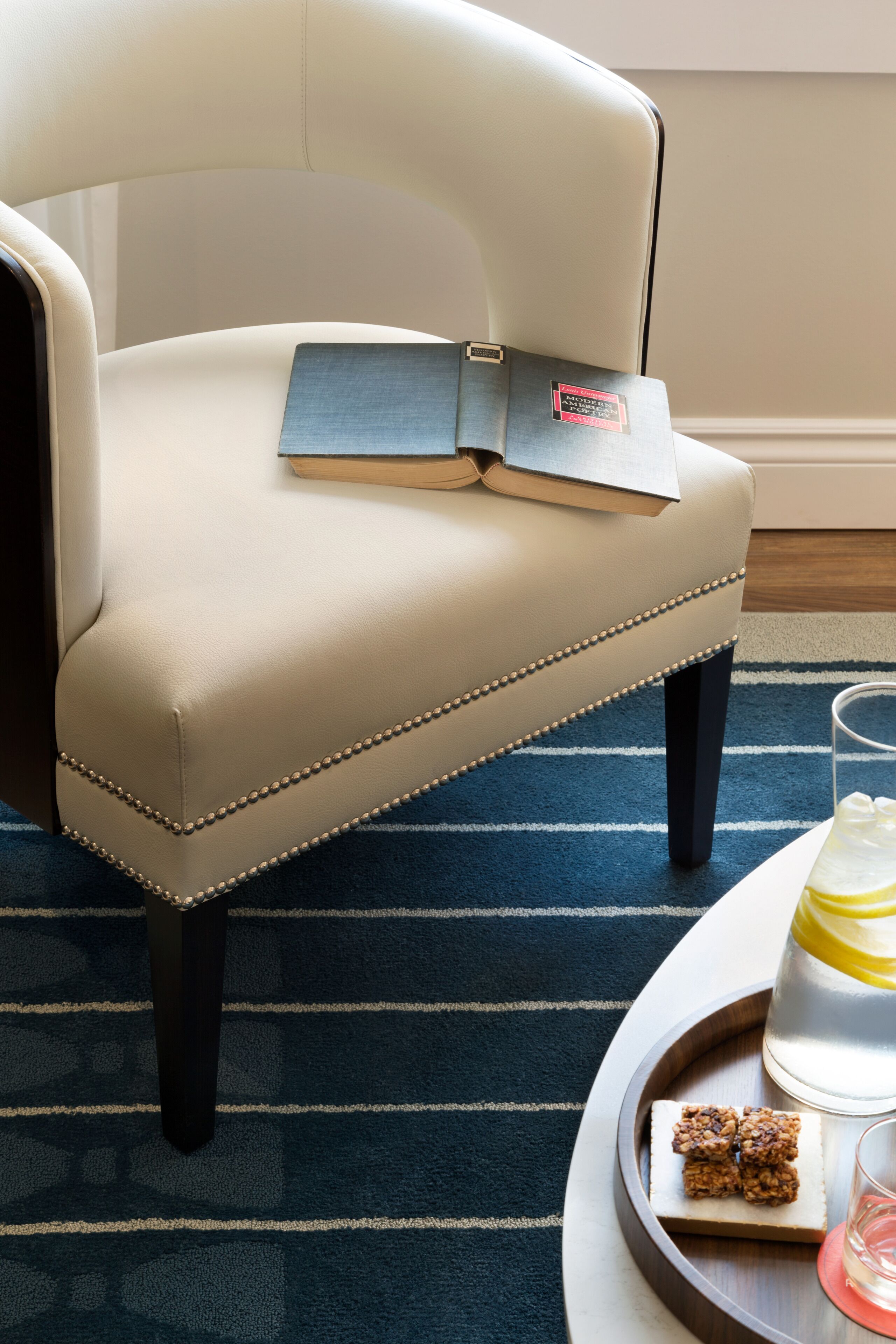 A beige upholstered chair with a book and a tray with a glass of water and snacks.