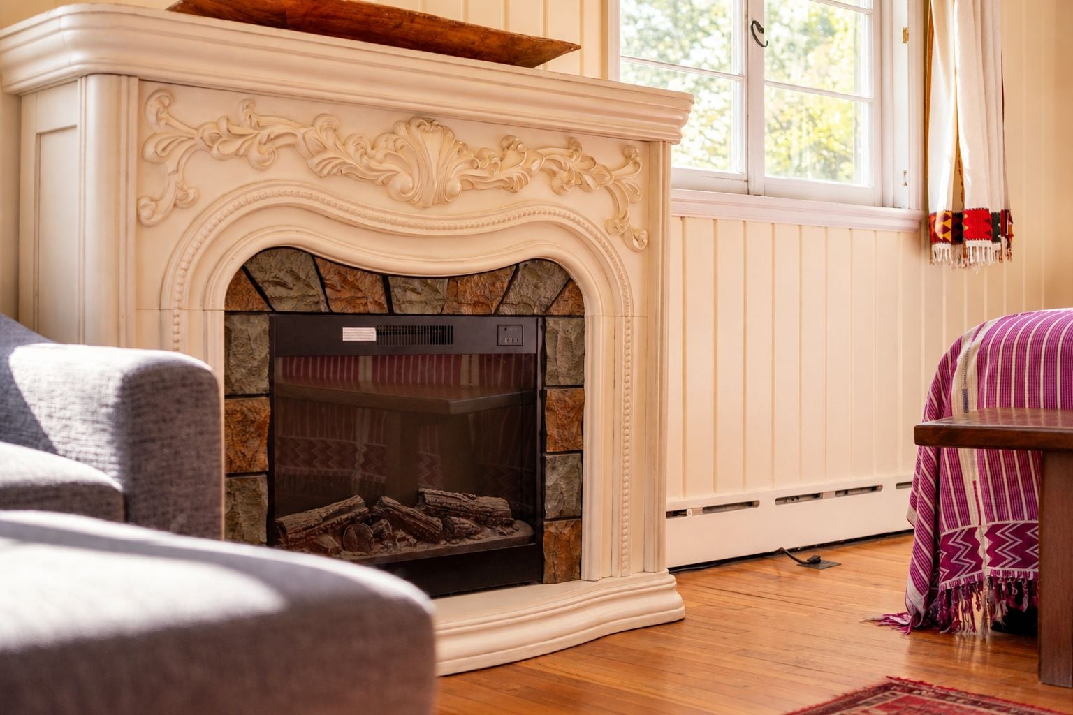 A fireplace with a stone surround, a grey sofa, and a patterned throw blanket.